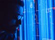 Hombre con lentes de tecnología observando pantallas de servidores o código con luces azules
