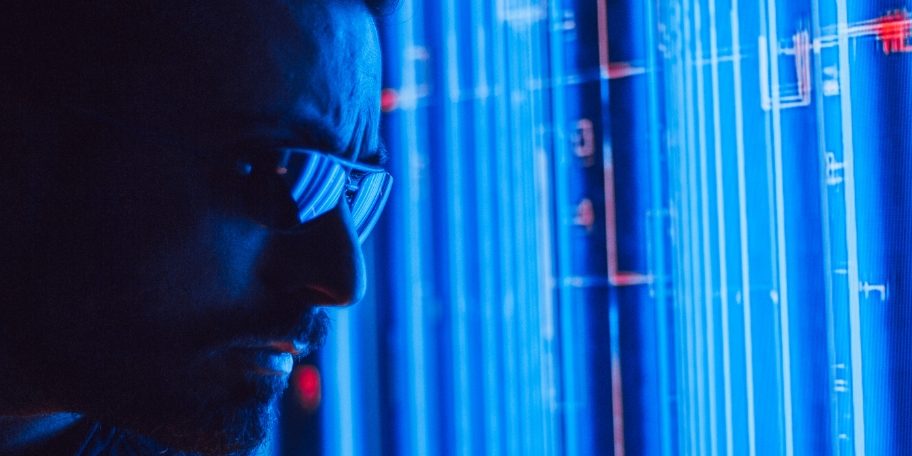 Hombre con lentes de tecnología observando pantallas de servidores o código con luces azules